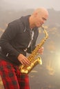 A bald man plays on a gold alto saxophone in the nature, against Royalty Free Stock Photo