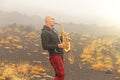 A bald man plays on a gold alto saxophone in the nature, against Royalty Free Stock Photo