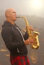 A bald man plays on a gold alto saxophone in the nature, against Royalty Free Stock Photo