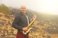 A bald man plays on a gold alto saxophone in the nature, against Royalty Free Stock Photo