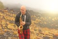 A bald man plays on a gold alto saxophone in the nature, against Royalty Free Stock Photo