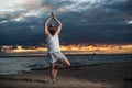 A bald man with a red beard practices yoga on the beach at sunset. A funny dude in a T-shirt and sunglasses meditates on Royalty Free Stock Photo