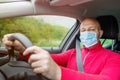 Bald man in red shirt driving car in face mask, Model holding driving wheel and looking at the camera