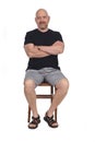 Bald man with sandals t-shirt and shorts sitting on white background, arms crossed Royalty Free Stock Photo