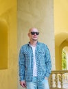 The bald man in sunglasses in a shirt and jeans.