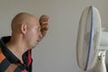 Bald man sweating because summer heat haze. Man refreshing in front of air electric fan Royalty Free Stock Photo