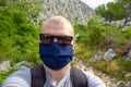 Bald man wearing black sunglasses and a blue facemask taking a selfie while trekking, hiking in nature in Croatia. Exploring the