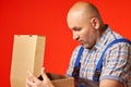 Bald man in work clothes opens an empty cardboard box and is very surprised