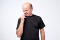 Bald mature man in black t-shirt smelling something unpleasant and bad