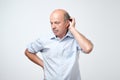 Bald mature man with mustache in blue shirt is suffering from indecision. Royalty Free Stock Photo