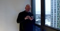 A bald middle-aged man is on a spacious balcony with large Windows, he is holding a mobile phone, looking at it leaning Royalty Free Stock Photo
