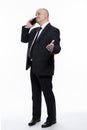 A bald middle-aged man in a strict black suit is standing and talking on the phone. Business success and complexity. White Royalty Free Stock Photo