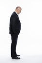 A bald middle-aged man in a strict black suit stands and looks down, holding his hands in his pockets. Business complexities. Side Royalty Free Stock Photo