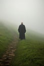 a bald priest wearing a black Chasuble. walking alone in a stone path on a cliff mountain.