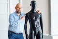 Bald serious adult man with beard, holding shoulders naked plastic black manikin Royalty Free Stock Photo