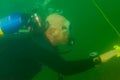 A bald SCUBA diver exploring a murky inland lake with dive flag line in hand