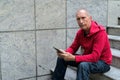 Bald senior man thinking and holding digital tablet while sittin