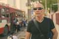 Bald senior tourist man thinking while wearing sunglasses at the bus stop in Bangkok Thailand Royalty Free Stock Photo