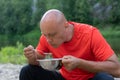 A bald sportsman in a red t-shirt is holding a metal bowl with soup and a spoon. Army lunch