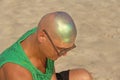 A bald and unusual young man, a freak, with a shiny bald head and round wooden glasses on the background of the beach and the sea