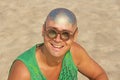 A bald and unusual young man, a freak, with a shiny bald head and round wooden glasses on the background of the beach and the sea