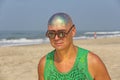 A bald and unusual young man, a freak, with a shiny bald head and round wooden glasses on the background of the beach and the sea