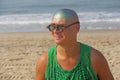 A bald and unusual young man, a freak, with a shiny bald head and round wooden glasses on the background of the beach and the sea