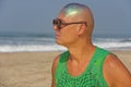 A bald and unusual young man, a freak, with a shiny bald head and round wooden glasses on the background of the beach and the sea