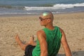 A bald and unusual young man, a freak, with a shiny bald head and round wooden glasses on the background of the beach and the sea