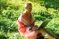 A bald woman in a bathrobe sits on green grass with a laptop in her hands. Online work, freelance concept. Sunny day Royalty Free Stock Photo