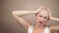 Bald woman holds her hands behind her head and screams. beige background, copy space Royalty Free Stock Photo