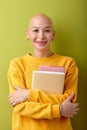 bald young woman looking at camera holding books in hands, alopecia and cancer