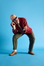 Balded man with mustache wear in vintage style bent over and talking on retro phone with call-sign over blue background.