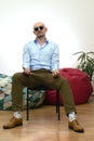 Bald bearded brutal macho or gangster man in sunglasses sitting on chair looking at camera. Confidence, individuality, masculinity Royalty Free Stock Photo