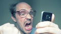 A balding man with glasses uses a smartphone. gesture surprise victory. Humor