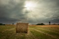 A bale of hay in the meadow and the glow of the sun from behind grey clouds Royalty Free Stock Photo