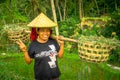 BALI, INDONESIA - APRIL 05, 2017: Women walk in the rice fields wearing a rice hat and holding with her hands a stick