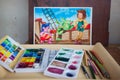 Bali, Indonesia - May, 16, 2022: Watercolor paints in a box and plastic palette on a tray with paintbrushes and pencils