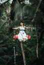 BALI, INDONESIA - MAY 16, 2018: Young woman swings in the jungle of Bali island. Rainforest of Indonesia. Travel concept