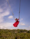 Bali swing trend. Caucasian woman in long red dress swinging in the jungle rainforest. Vacation in Asia. Travel lifestyle. Blue Royalty Free Stock Photo