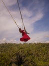 Bali swing trend. Caucasian woman in long red dress swinging in the jungle rainforest. Vacation in Asia. Travel lifestyle. Blue Royalty Free Stock Photo