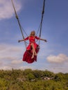 Bali swing trend. Caucasian woman in long red dress swinging in the jungle rainforest. Vacation in Asia. Travel lifestyle. Blue Royalty Free Stock Photo