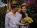 Balinese culture. Portrait of multicultural couple wearing Balinese clothing. Charming woman holding fan. Caucasian wife and