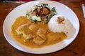 Balinese dinner served in a white plate with yellow gravy on top of the meat and vegetable