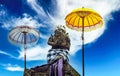 Balinese hindu mythological lord shiva stone figure between two traditional ceremonial umbrellas tedung, blue sky white clouds