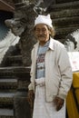 Balinese Man Standing Next To A Dragon Carved Head At The Entrance Of Merajan Hindu Temple At