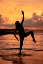 A Balinese woman in the form of a silhouette performs ballet movements very deftly and flexibly on the beach with the waves