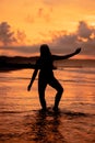 A Balinese woman in the form of a silhouette performs ballet movements very deftly and flexibly on the beach with the waves