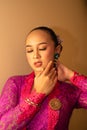 Balinese Women showing their green earrings while wearing a pink traditional dress