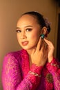 Balinese Women showing their green earrings while wearing a pink traditional dress